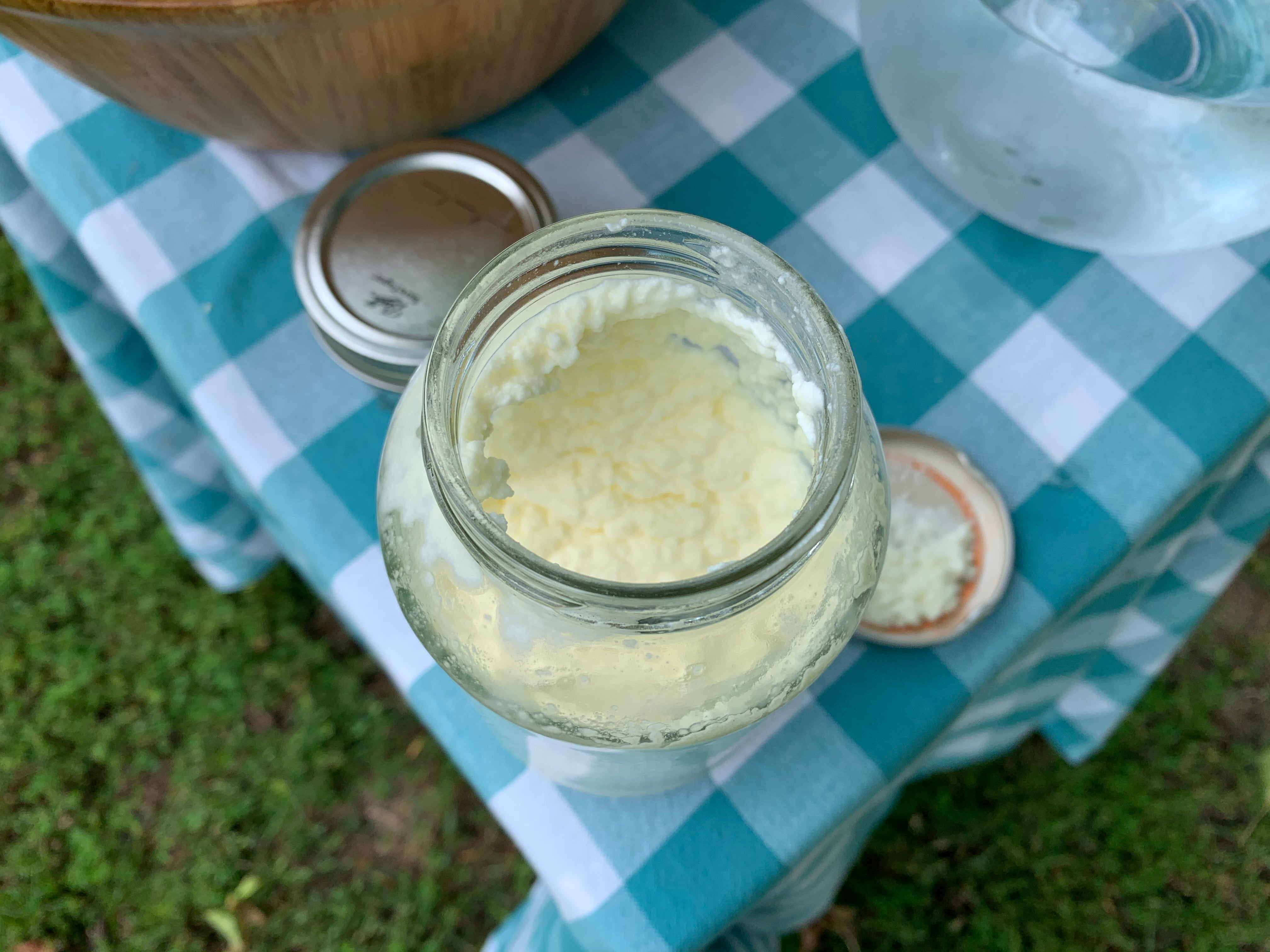 On a table there is a mason jar filled with cream that has the texture of ricotta cheese.